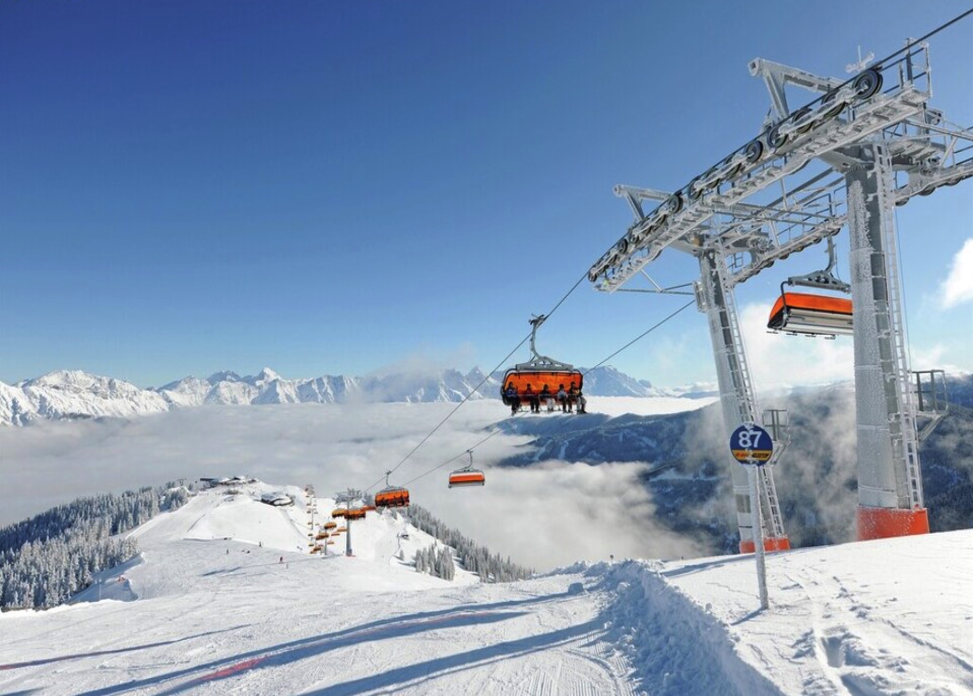 Zomerstoelenlift met skiërs in de bergen, omgeven door sneeuw en wolken, met een panoramisch uitzicht op de bergtoppen.